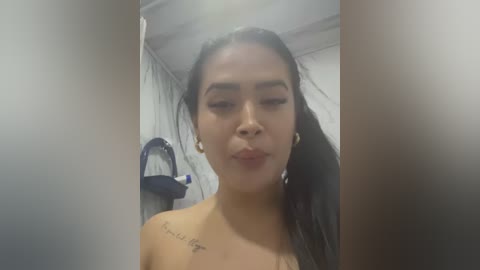 Media: Video of a Latina woman with medium skin tone, long dark hair, and a tattoo on her shoulder. She is indoors, wearing makeup, and has a neutral expression.