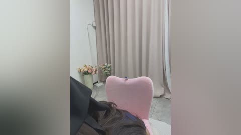 Media: Video of a minimalist room with a beige curtain, a pink chair, a vase of flowers, and a tall floor lamp.