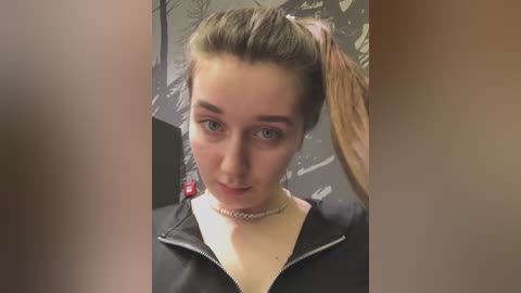 Media: Video of a young woman with fair skin, brown hair in a high ponytail, wearing a black jacket over a beige turtleneck, against a blurred, abstract, dark background.