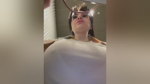 Media: A video of a young woman with fair skin and brown hair, wearing a white shirt, captured from a low angle through a circular mirror, showcasing her chest and upper body.