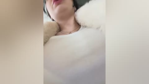 Media: Video of a woman with light skin and short dark hair, wearing a white fluffy coat and a red lip, taken from a low angle.