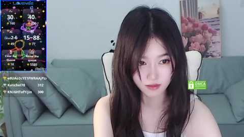 Media: A video of a young Asian woman with long black hair, fair skin, and a neutral expression, sitting on a gray sofa. A weather app screen shows rain and temperatures in the background.