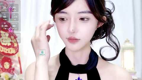 Media: Video of a young Asian woman with pale skin and dark hair styled in a side ponytail, wearing a black halter top and a silver nose ring, adjusting her hair in front of a blurred, colorful background.