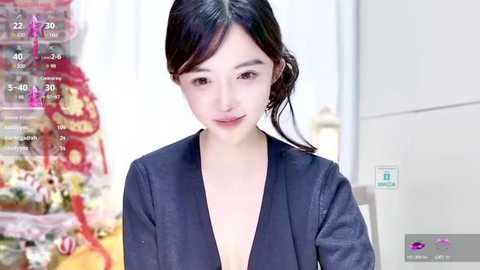 Media: A video of an East Asian woman with fair skin, dark hair, and a nose ring, wearing a black V-neck top, standing indoors against a blurred background.