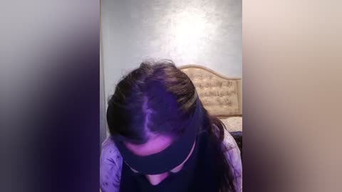 Media: A video shows a woman with long, dark hair, wearing a black blindfold and a light floral-patterned shirt, standing in a room with a beige headboard and a silver wall.