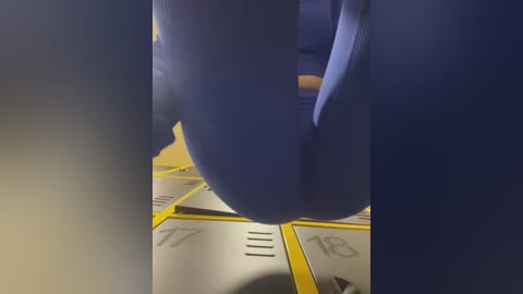 Media: A close-up video of a blue-clad person's legs and feet, with a yellow and black tiled floor visible beneath. The focus is on the legs, emphasizing their position.