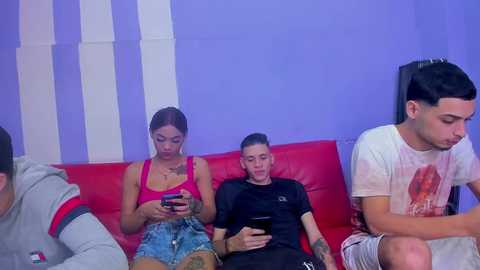 Media: Video of four young people on a red couch in a room with purple walls, playing video games.