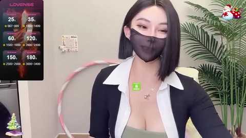 Media: A video of a young East Asian woman with a black bob haircut, wearing a black mask, black blazer, and a revealing white shirt, in an indoor setting with a potted plant.