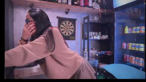 Media: A video of a young woman with long black hair, wearing a beige sweater, leaning over a pool table in a dimly lit, cluttered pool hall.