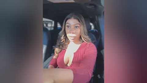 Media: Video of a young woman with long brown hair, wearing a low-cut red top, sitting in a car with dark interior, looking surprised and slightly open-mouthed.