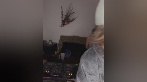 Media: Video of a woman in a white dress standing near a DJ booth with a DJ mixer and speakers, featuring a Christmas wreath on a white wall.