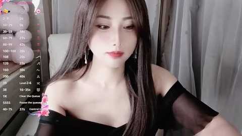 Media: A video of a young Asian woman with long, straight black hair, fair skin, and a slender physique. She wears a black off-shoulder top and silver earrings, looking seductively into the camera. The background features a teddy bear and a digital calendar.