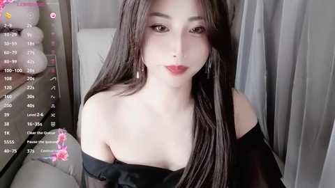 Media: A video of a young East Asian woman with long, straight black hair, fair skin, and red lipstick, wearing an off-shoulder black dress. She has a soft, neutral expression.