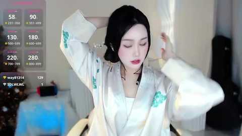 Media: Video of a young East Asian woman with fair skin, black hair, and red lipstick, wearing a white robe with green floral print, adjusting her hair in a dimly lit room.