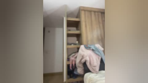 A blurred video of a messy bedroom with a wooden wardrobe, clothes on the floor, and a beige curtain partially drawn.