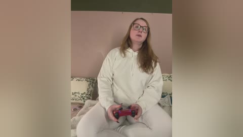 Media: Video of a plus-size woman with glasses, long red hair, white hoodie, and pants, sitting on a floral-patterned couch, holding a red game controller, indoors with pastel-colored walls.