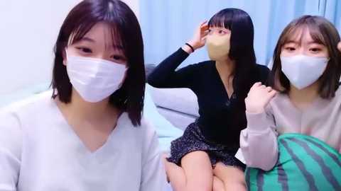 Media: Video of three East Asian women with masks, wearing casual clothing, one with a striped blanket, in a modern, lightly-colored room.