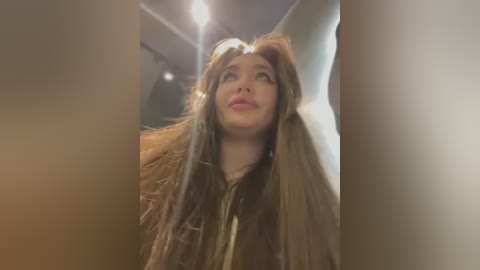 Media: A video of a young woman with long, messy brown hair, wearing a brown jacket, looking upwards with a dreamy expression. The background is blurred, creating a soft focus effect.