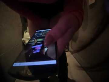 Media: Video of a person, likely male, wearing a red shirt, using a small, black, lit-up screen device with a keyboard. The background is dimly lit, showing a cluttered desk with indistinct objects.