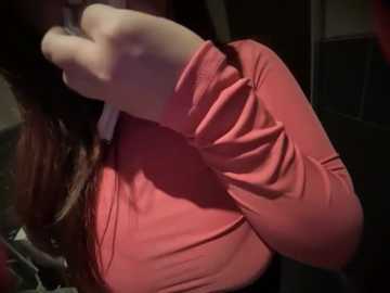 Media: A close-up video of a person's left arm in a long-sleeved, pink, ribbed sweater, with light brown hair partially visible. The background is dimly lit, with indistinct objects.