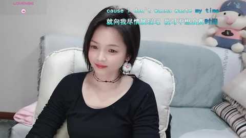 Media: Video of a young East Asian woman with straight black hair, wearing a black top and choker, sitting on a white chair in a pastel-colored room. Text overlays in Chinese.