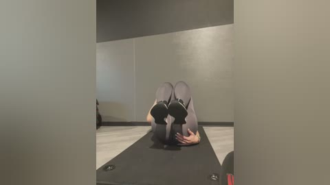 Media: Video of a person in a yoga pose on a black and white striped yoga mat in a dimly lit room with light grey walls.