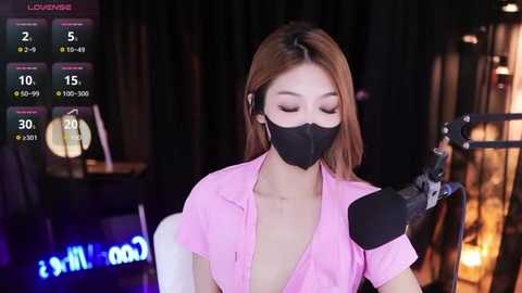 Media: Video of an Asian woman with long, straight brown hair, wearing a pink shirt, black gloves, and mask, holding a syringe, in a dimly lit room with a digital timer screen.