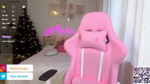 Media: A video shows a pink gaming chair with a plush pillow in a cozy, softly lit room. The background features a decorated Christmas tree, framed art, and a bed with a white blanket.