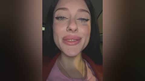 Media: Video of a young woman with fair skin, dark hair, and facial piercings, wearing a red jacket, smiling with closed eyes.