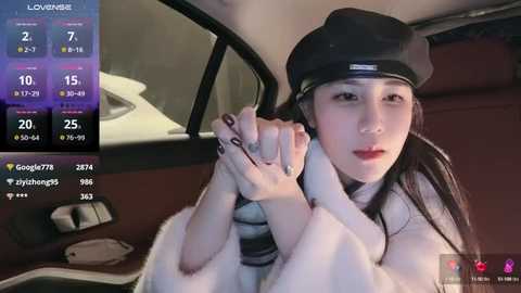 Media: Video of an Asian woman in a black cap and striped top, hands clasped, seated in a car. Background shows a smartphone screen with weather and location details.