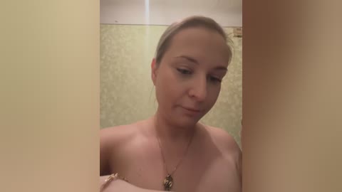 Media: Video of a fair-skinned woman with brown hair, wearing a strapless top, standing in a bathroom with a beige wall and floral wallpaper.