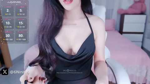 Media: Video of an East Asian woman with long black hair, wearing a black halter top, sitting on a bed in a bedroom.