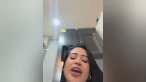 Video of a young woman with long black hair, medium skin tone, wearing a black top, lying on a treadmill in a gym with beige walls and equipment, her eyes closed in a relaxed or possibly asleep state.