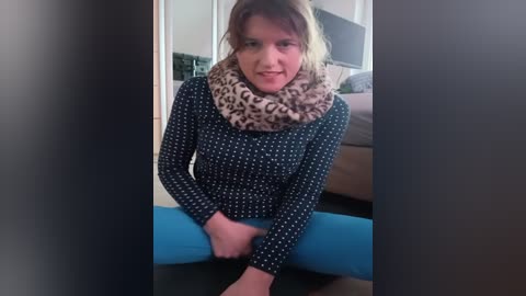 Media: A video of a woman in a leopard-print scarf and blue leggings, sitting on a blue yoga mat, with a beige sofa and TV in the background.