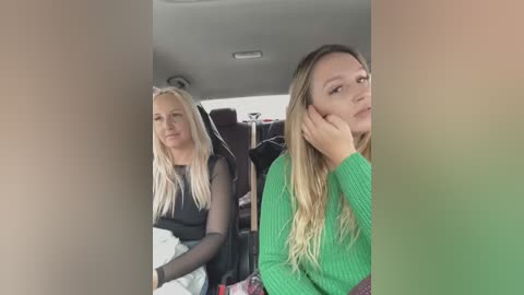 Media: Video of two blonde women in a car, one in a black top, the other in a green sweater, seated next to each other, looking ahead, with blurred background.