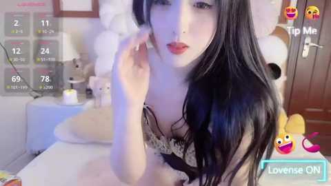 Media: Video of an Asian woman with long black hair, fair skin, and red lipstick, wearing a sheer black lace bra, in a cozy bedroom with plush toys and a bed.