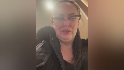 Media: Video of a middle-aged woman with glasses, wearing a black jacket, indoors with soft lighting.