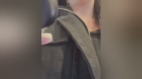 Media: A blurry video of a person wearing a black leather jacket with a visible seatbelt, partially obscured by out-of-focus objects. The person's face is not visible, and the background is indistinct.