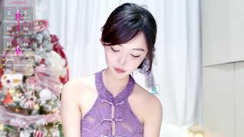 Media: Video of a young East Asian woman with fair skin and dark hair in a purple, lace, halterneck dress, standing in front of a decorated Christmas tree.