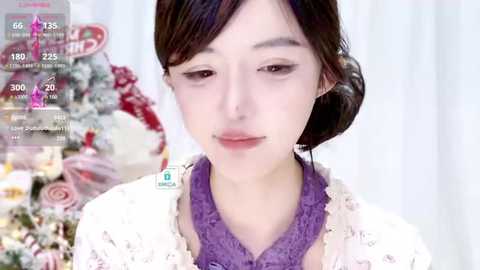 Media: Video of a young Asian woman with fair skin and dark hair, wearing a purple top and white lace cardigan. Background features festive decorations and a virtual camera overlay.