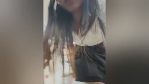 Media: A blurred video of a young woman with long, dark braided hair, wearing a black top with a white collar, against a blurred background.