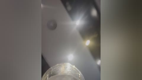 Media: A video showing a close-up of a glass beaker with a blurry, glowing light source behind it, creating a bokeh effect. The beaker's transparent and shiny, reflecting the light.