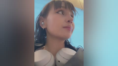 Media: Video of a young woman with brown hair, wearing white headphones, looking upward with a contemplative expression, against a blue background.