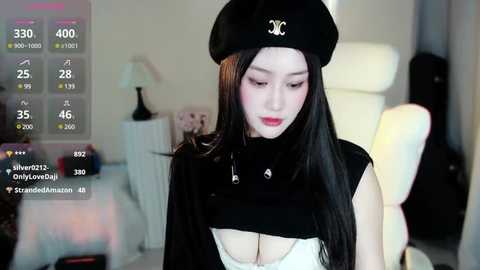 Media: A video of an Asian woman with long black hair, fair skin, and a black beret. She wears a revealing black top, revealing cleavage, in a modern, minimalist room with a white chair and lamp.