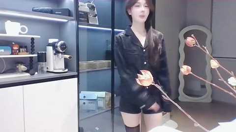 Media: Video of an Asian woman with long black hair in a black leather jacket, holding a spinning wooden top in a modern kitchen with glass cabinets and a white counter.