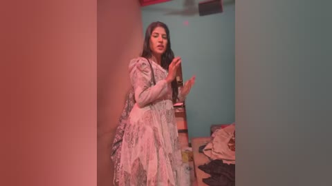 Media: Video of a woman in a vintage, floral-patterned dress, dancing in a dimly lit, cluttered room with teal walls and a messy bed.