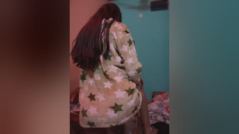 Media: A video of a person with long dark hair wearing a star-patterned pajama top, standing in a dimly lit room with teal walls and scattered clothes on the floor.