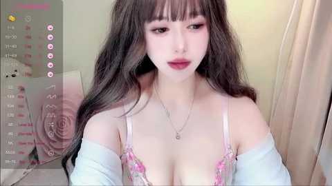 Media: A video of a young Asian woman with long, dark hair, wearing pink lingerie and a white off-shoulder top, posing indoors with a soft, pastel background.