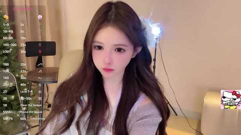 Video of a young woman with long brown hair, wearing a light grey sweater, seated in a living room with a Christmas tree and smartphone recording her.