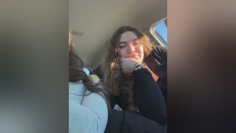 Media: Video of a woman with long, curly brown hair, wearing a black top, resting her head on a window in a car, with sunlight creating a soft, warm glow.